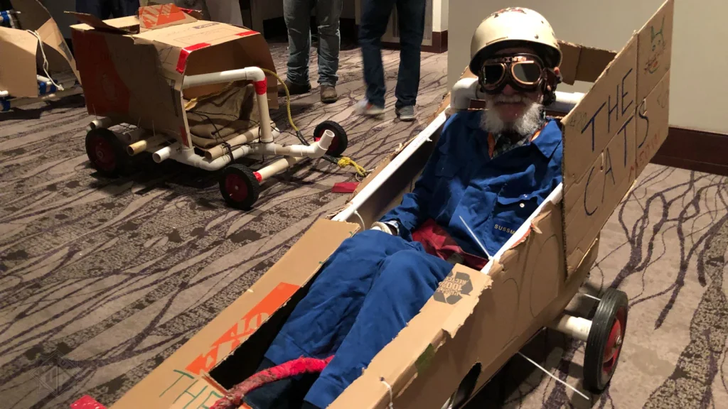 Participant sits in a handmade cardboard race car during Venture Up's Create-A-Craft Cars team-building activity.