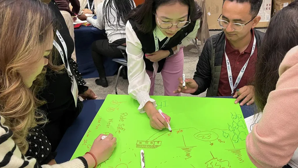 Group of people around a bright green poster, drawing with markers during a collaborative workshop.