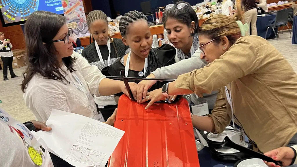 Group of diverse women gathered around a bright red device, adjusting its frame during a hands-on workshop. | Team Building Activities & Techniques