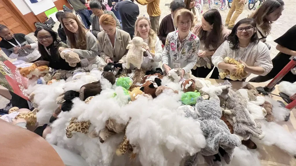 Group of people at a plush toy drive, selecting stuffed animals from a large pile of toys.