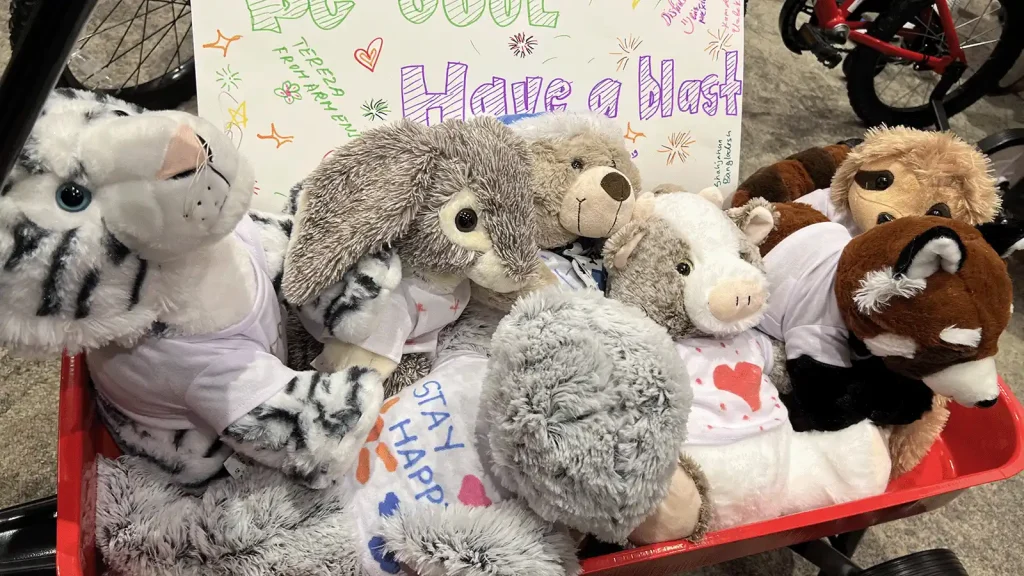 Several plush stuffed animals piled in a red wagon, with a colorful hand-drawn sign reading 'Have a blast' in the background.