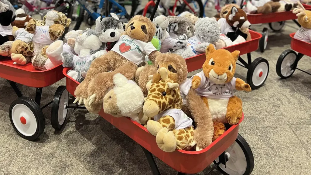 Red wagons overflowing with stuffed animals (teddy bears, giraffe, lion) ready for donation or display at a toy drive.