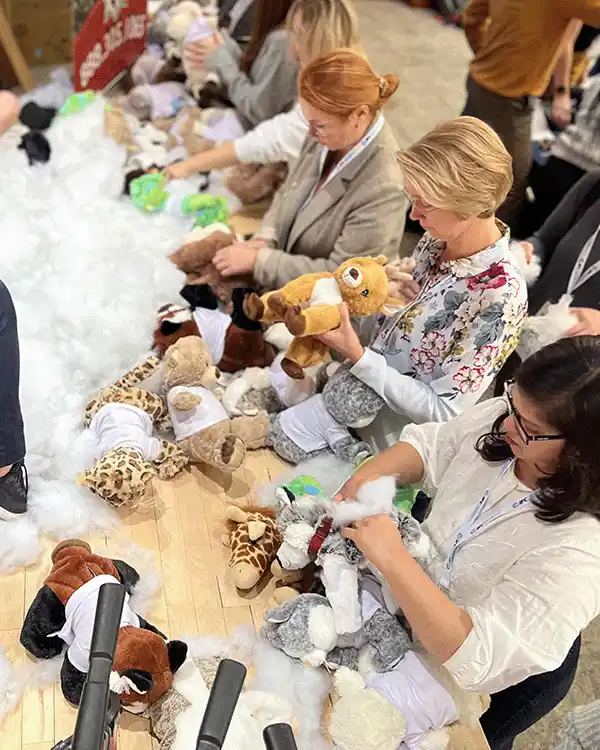 People at a plush-toy stuffing station, filling and assembling stuffed animals from piles of toys and cotton fluff. | Team Building Activities & Techniques
